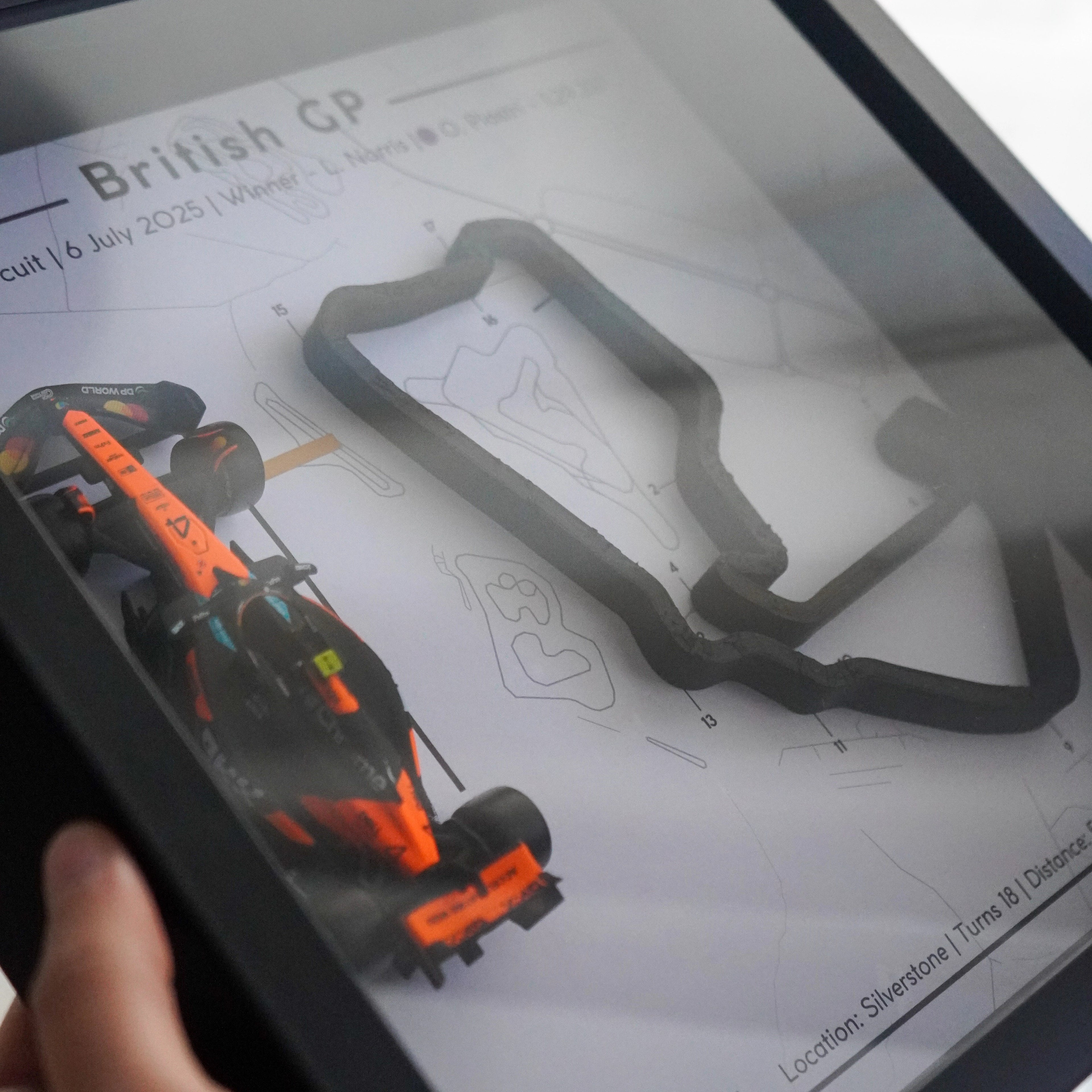 Person holding a tablet displaying a Formula 1 car and track layout on a screen.